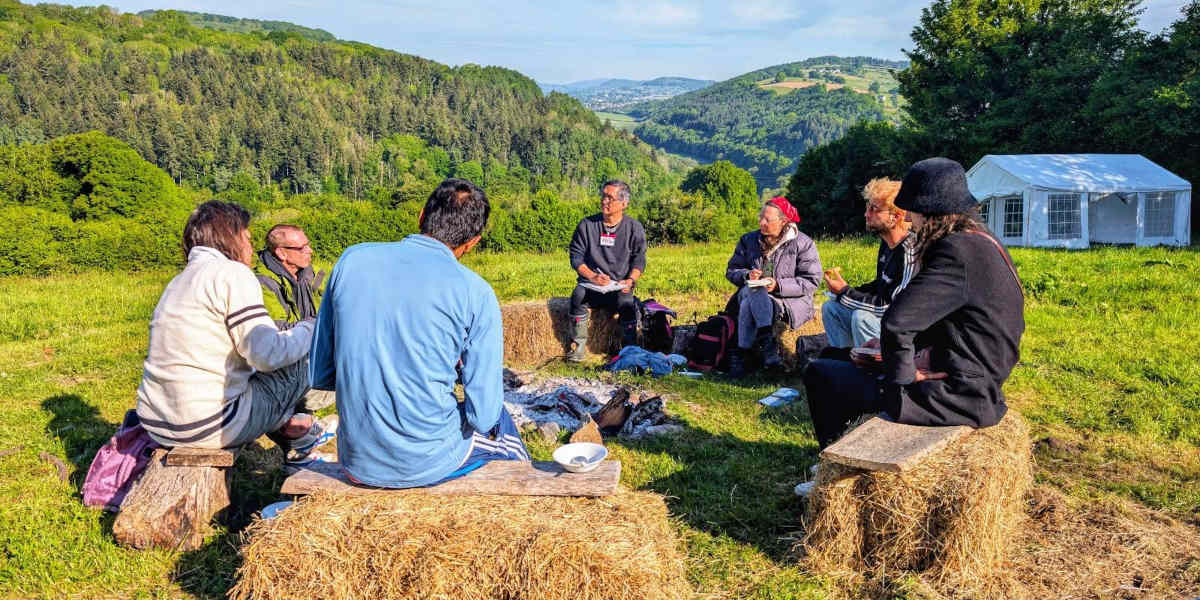 Six people sat on hay bales talking in a circle overlooking a rural valley